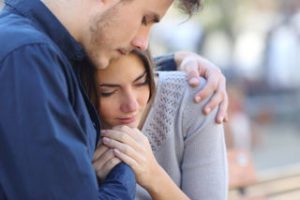 Una mujer visiblemente afectada se apoya en un hombre que la abraza con cariño, mostrando el apoyo humano Fundación porqueViven