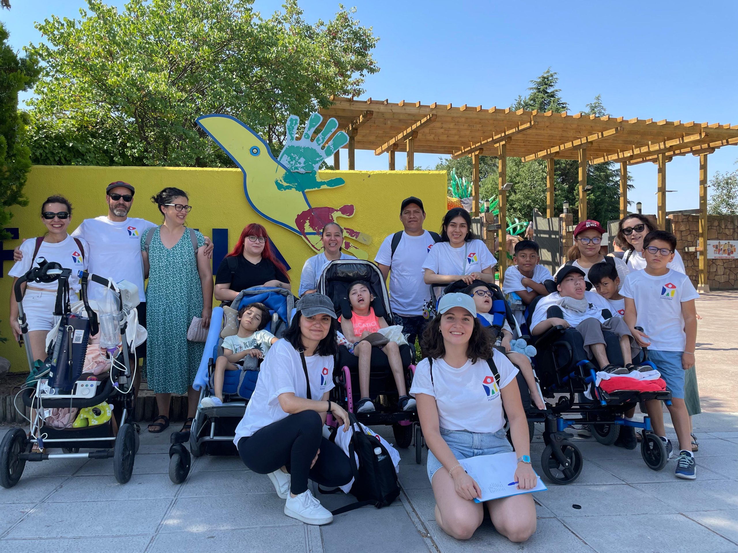 Equipo Fundación porqueViven, adultos y niños (algunos en silla de ruedas), posan juntos frente a mural con huellas