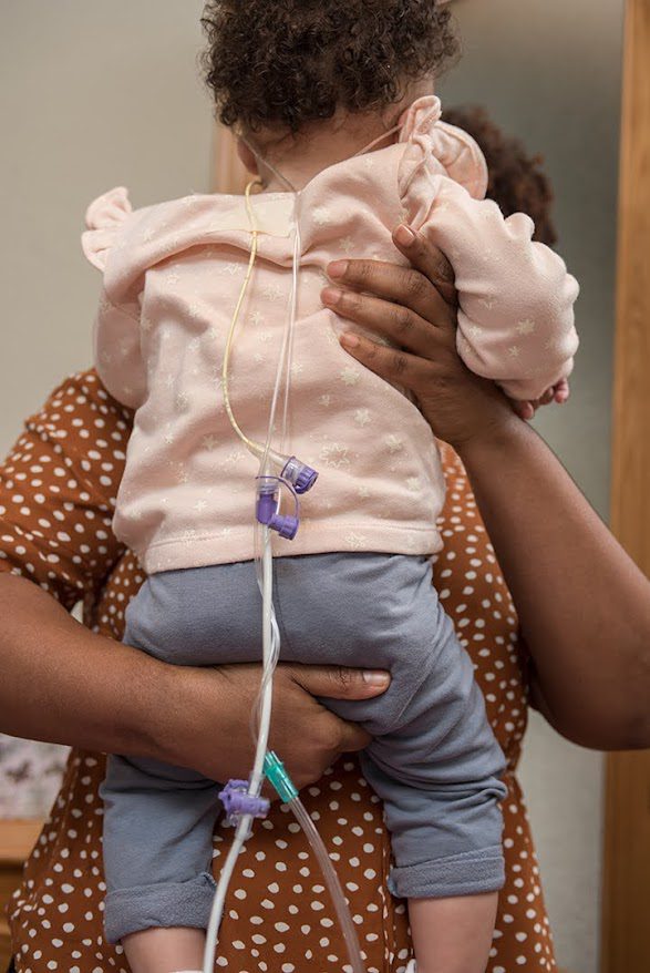 Un adulto sostiene a un niño pequeño con sondas médicas, ambos con ropa de lunares; atención