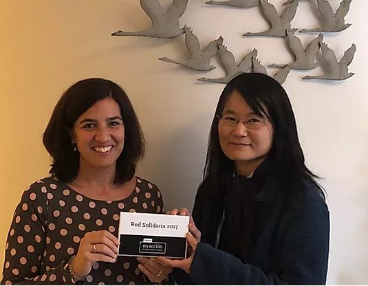 Dos mujeres sonríen en un espacio interior junto a una placa Red Solidaria 2017, representando