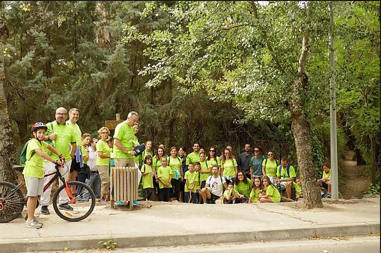 Grupo de personas con camisetas verdes Fundación porqueViven, junto a un bosque en Madrid; una niña con casco y bici delante