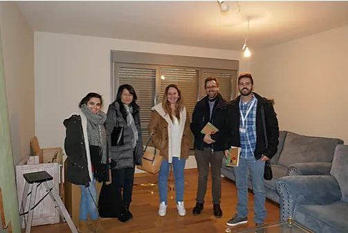 Equipo Fundación porqueViven, en Madrid, sonríe en una sala luminosa con sofá y mesas, sosteniendo alfombras de trabajo
