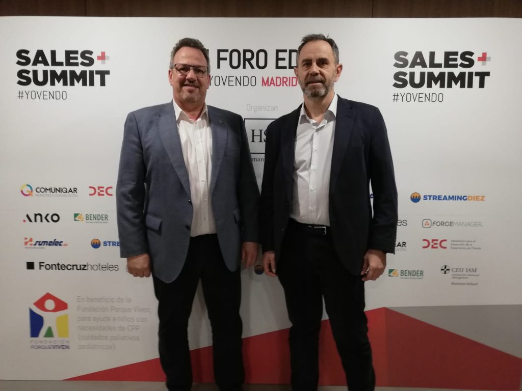 Dos profesionales del sector, vestidos de manera formal, posan juntos ante un fondo de la en un evento