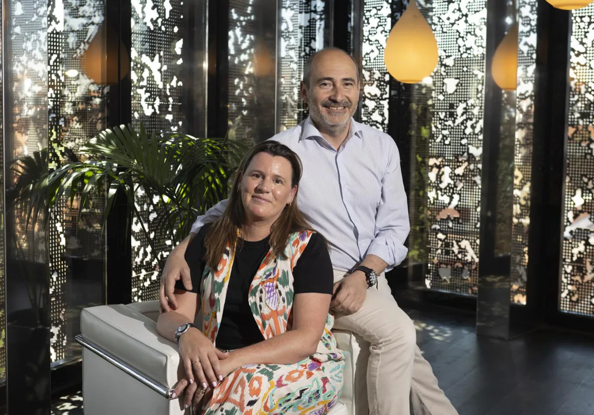 En la imagen, una mujer sentada sonríe junto a un hombre de pie que le acompaña con calidez; ambos representan al equipo , dedicados