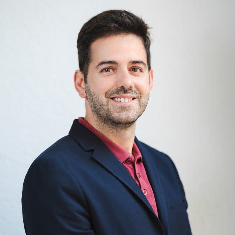 Un hombre sonriente, con barba cuidada y blazer azul, representa a en cuidados paliativos pediátricos