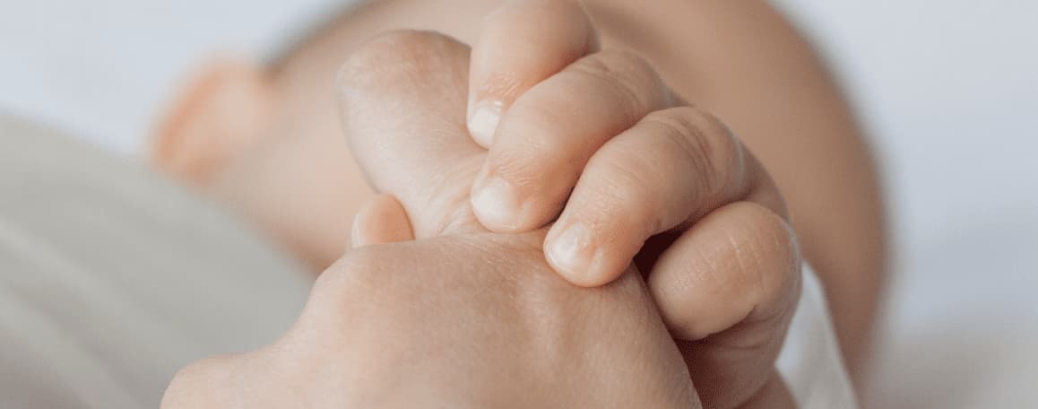 Primer plano de la mano de un bebé aferrada a un dedo adulto, reflejando el apoyo y cuidado pediátrico Fundación porqueViven