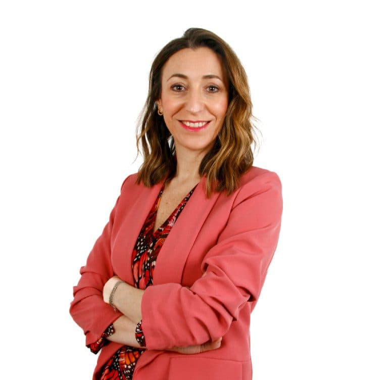 Una mujer sonriente apoya a , con blazer rosa y fondo blanco