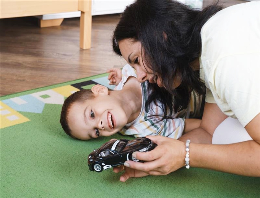 Una mujer y un niño sonríen jugando juntos en una alfombra verde, compartiendo apoyo emocional gracias