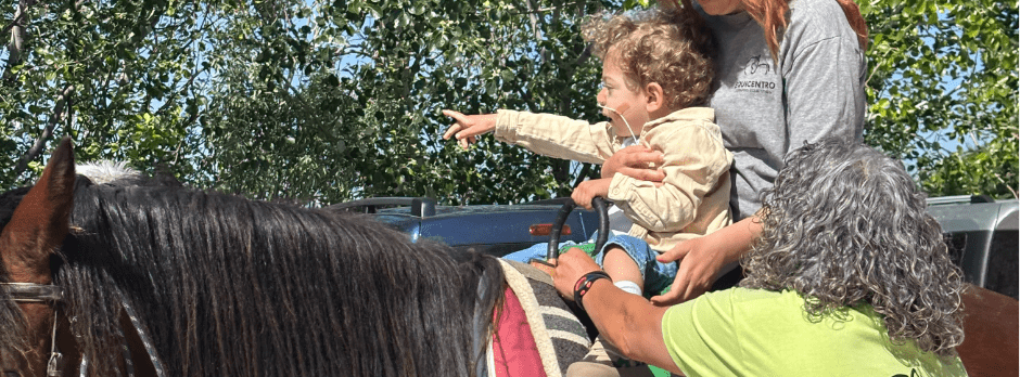 Niña sonriente en equinoterapia con , acompañada por dos adultos de apoyo. Ambiente al aire libre en Madrid